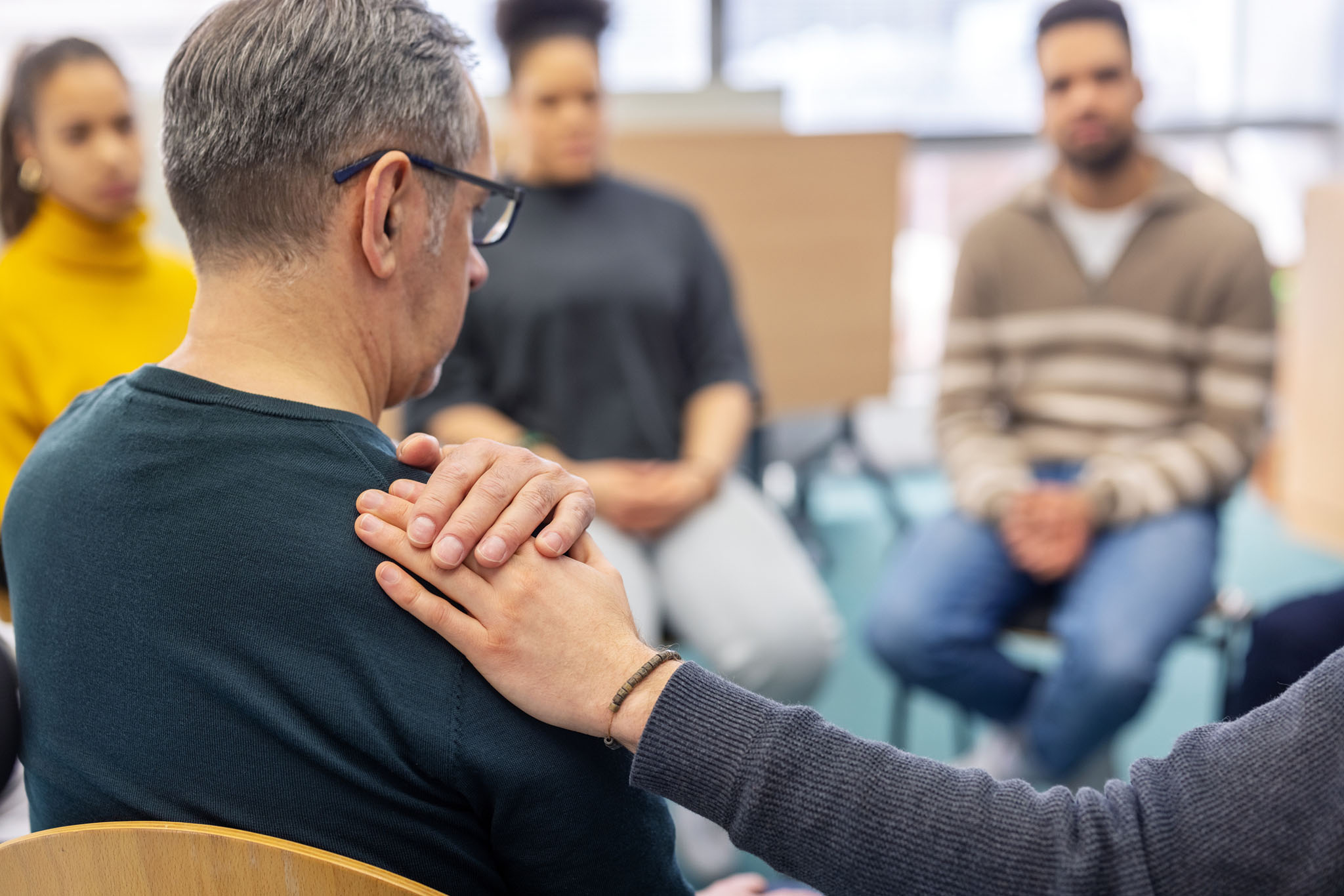 Senior man being comforted by another participant in group therapy at community center GettyImages 2171148861