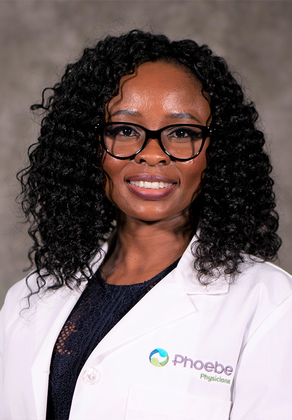 Gloria Esoimeme, MD, with curly hair and glasses, smiles in a white lab coat bearing the Phoebe Physicians logo, against a neutral background. Gloria Esoimeme, MD, with curly hair and glasses, smiles in a white lab coat bearing the Phoebe Physicians logo, against a neutral background.