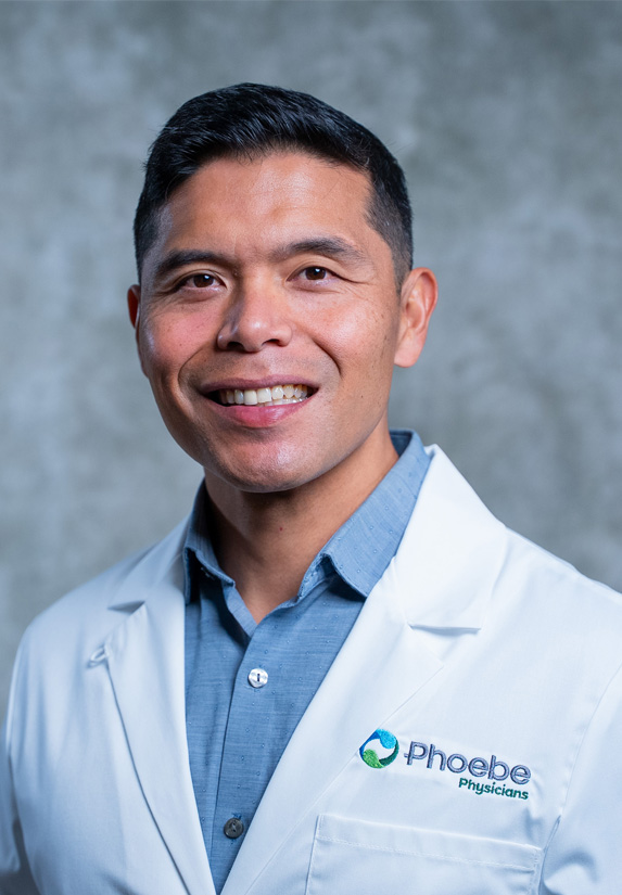Dr. Joseph Mariano, wearing a white lab coat with Phoebe Physicians logo, poses in front of a gray background. Dr. Joseph Mariano, wearing a white lab coat with Phoebe Physicians logo, poses in front of a gray background.