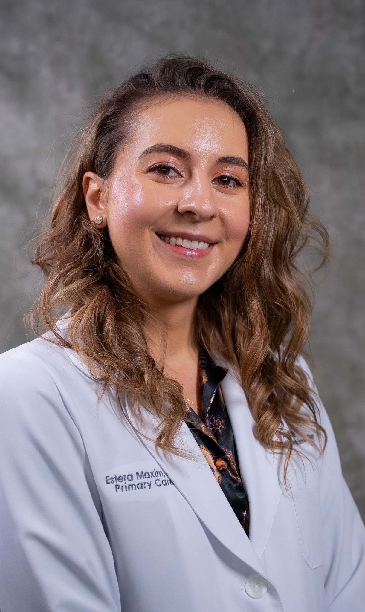 Smiling woman wearing a white medical coat stands in front of a gray background. Smiling woman wearing a white medical coat stands in front of a gray background.