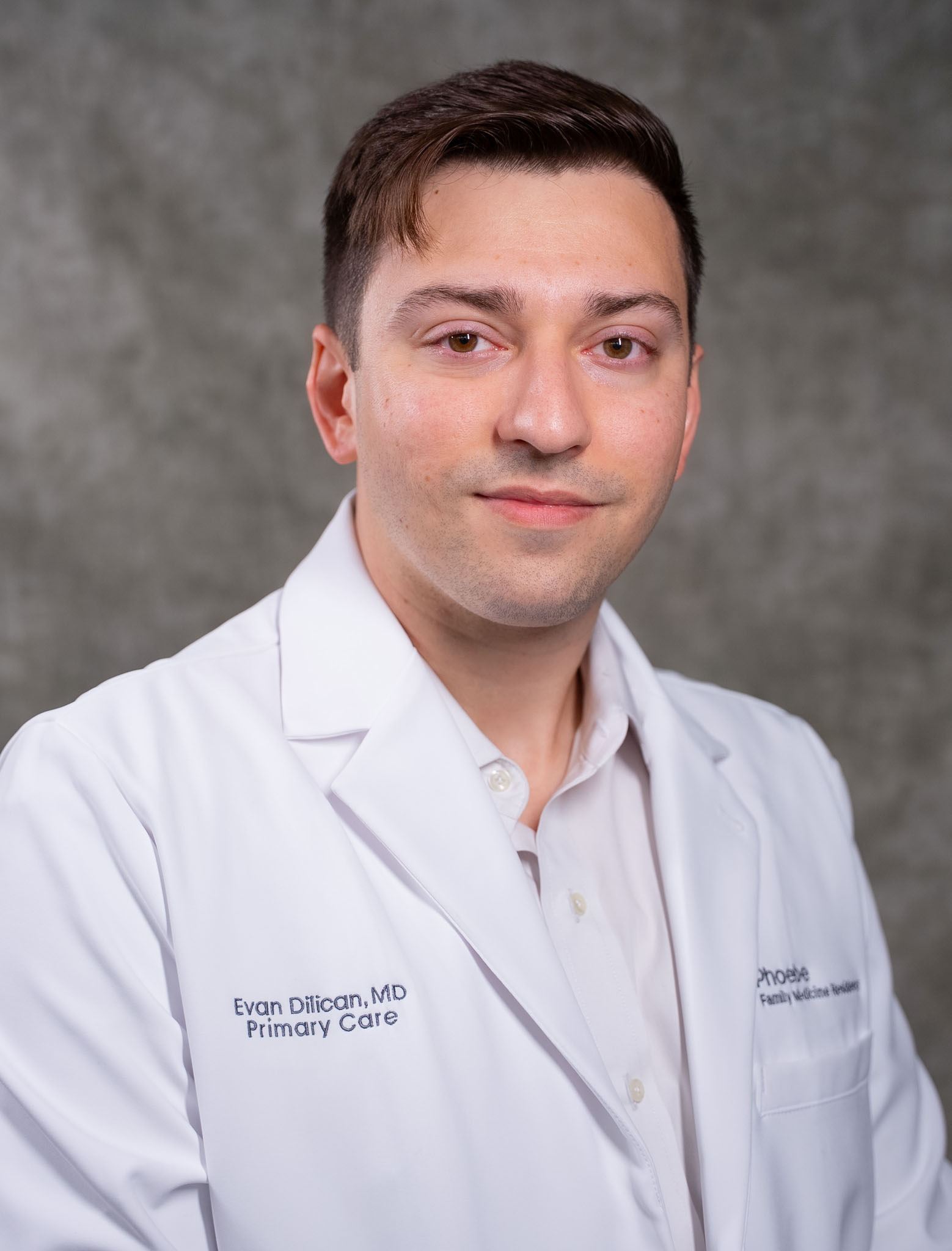 A man in a white medical coat poses for a professional portrait against a gray background. A man in a white medical coat poses for a professional portrait against a gray background.