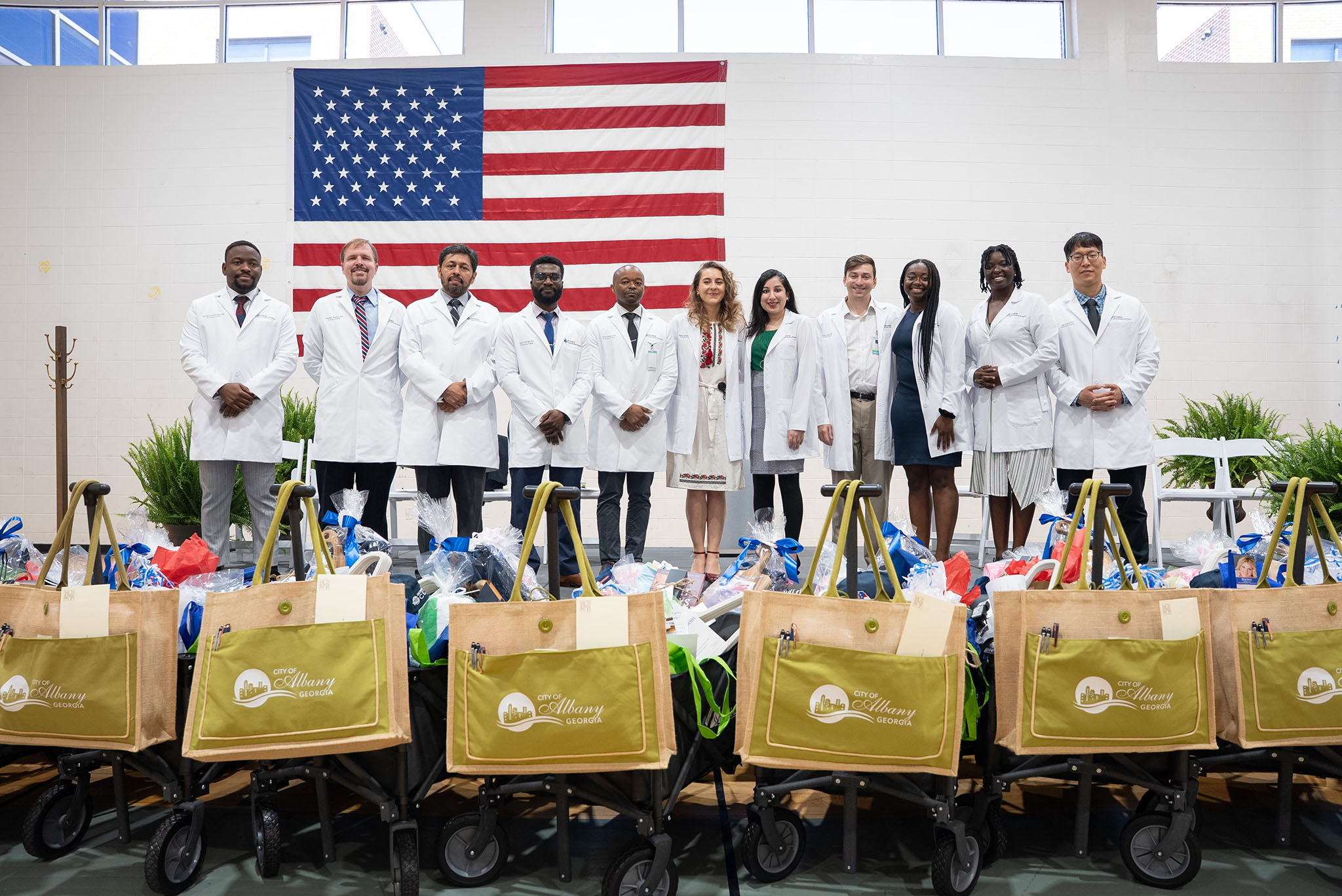 Ten people in white coats stand in front of an American flag, with carts of donated goods lined up before them. Ten people in white coats stand in front of an American flag, with carts of donated goods lined up before them.