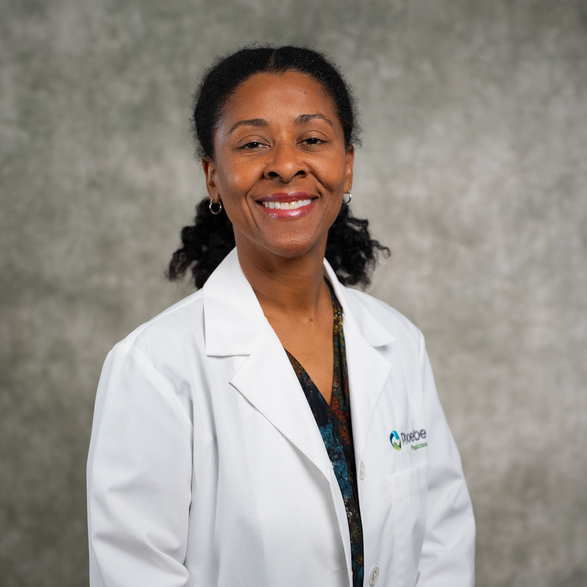 A woman in a white lab coat smiles confidently while standing before a neutral gray background. A woman in a white lab coat smiles confidently while standing before a neutral gray background.
