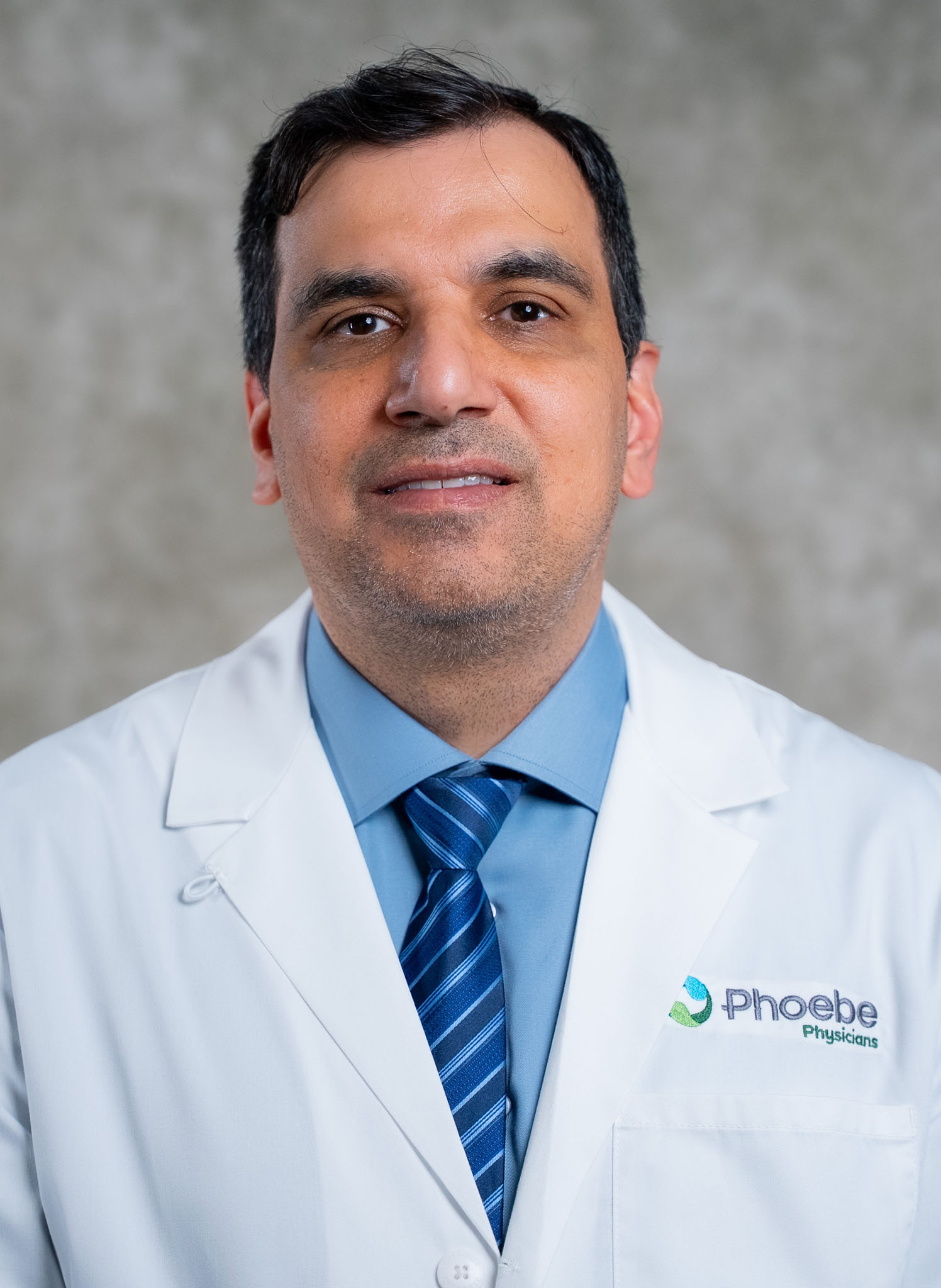 Moshrik Abd Alamir, in a white lab coat and blue tie, stands before a gray background wearing a Phoebe Physicians badge. Moshrik Abd Alamir, in a white lab coat and blue tie, stands before a gray background wearing a Phoebe Physicians badge.