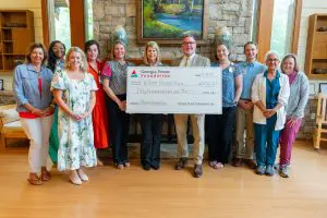 Thirteen people smile and stand indoors, holding a $50,000 check to William Harris Hom for Phoebe Hospice Services honoring Jimmy Carter.
