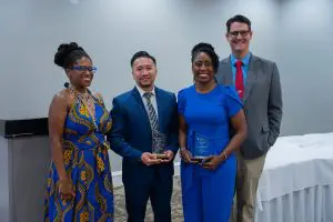 Four people indoors smile at the camera; two hold Outstanding Faculty awards from the Phoebe Family Medicine Residency program.