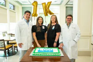Four medical professionals celebrate a surgery milestone at Phoebe Bariatrics with a "1000" cake and gold "1K" balloons.