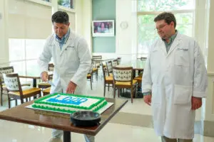 Two doctors in white coats cut a cake marked "1,000" at Phoebe Bariatrics, celebrating a bariatric surgery milestone for the organization.