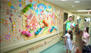 Colorful hospital hallway with flower art; a man and children smile, supporting the $30,000 Campaign for Children’s Miracle Network.