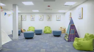 A bright room features green bean bags, blue stools, toys, and art.