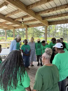 A group in green shirts stands in a circle under a pavilion, appearing to pray together