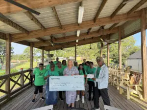 A group from Phoebe Worth and the community kitchen stands on a covered porch, smiling at the camera while holding an oversized $50,000 check.