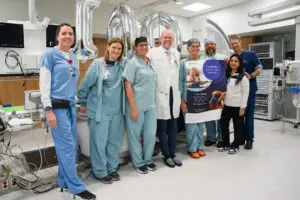 Eight medical professionals, including an electrophysiologist, pose with a celebratory banner for Phoebe’s advanced pacemaker success.