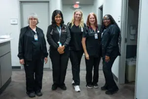 Five women in black scrubs smile together in a Primary Care clinic hallway at Laurel Place.