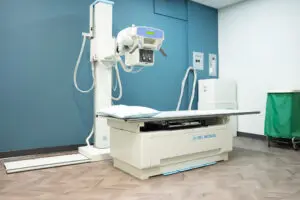 A hospital X-ray machine setup with patient table at Laurel Place, a clean, modern Primary Care medical room by Phoebe.