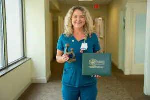 Smiling nurse in blue scrubs holds a DAISY Award trophy and green certificate, celebrating patient advocacy at Phoebe.