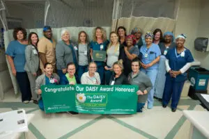 Healthcare workers display compassion, holding a DAISY Award banner and certificate together in the hospital.