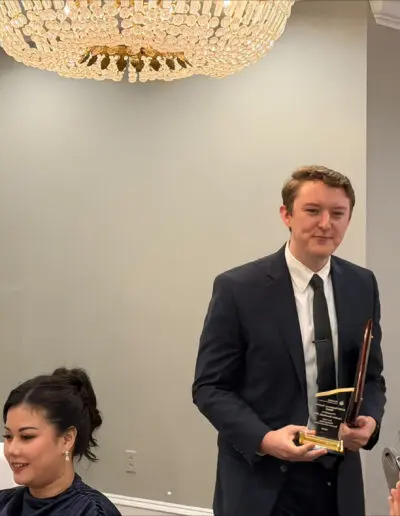 A man in a suit, one of the award recipients, walks past applauding guests at the Phoebe Family Medicine Residency Graduation Ceremony.