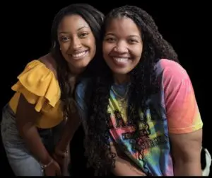 Tanique and Greta smile together in vibrant outfits, celebrating neonatal care against a black background.