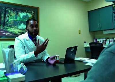 A doctor from Phoebe explains the 340B Program to a patient, holding a pill bottle amid brochures and medical supplies.