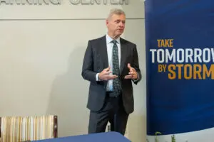 A man in a suit speaks, gesturing next to a sign about Southwest Georgia healthcare workforce partnership.