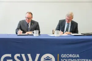 Two men in suits sign documents at a table, celebrating a new Southwest Georgia healthcare workforce development partnership.