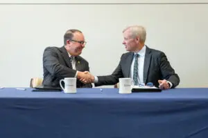 Two men in suits shake hands across a table, signifying a new healthcare partnership in Southwest Georgia.