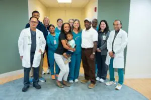 One Birthday Visit, Countless Acts of Kindness: Phoebe Medical Assistant Earns BEE Award 4 Doctors, nurses, and a family with a child smile together at the hospital after the Sumter Pink Walk for Cancer event.