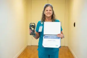 Woman in teal scrubs smiles, holding a certificate and black owl trophy after the Pink Walk for Cancer in Sumter on October 24.