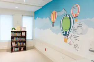 Children’s hospital room with bookshelf and vibrant NICU mural, celebrating families and babies reaching important milestones.