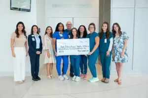 A group in medical attire holds a large check for the Phoebe Foundation, supporting NICU care for mothers and babies.