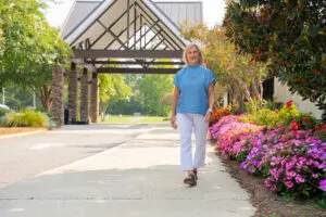 A woman strolls in faith along a garden path lined with pink flowers near a building with a covered entrance.