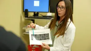 A doctor in a white coat discusses Alzheimer’s early detection and points to brain scans in a Dougherty County office.