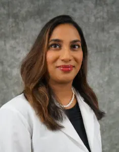 A person in a white coat and pearl necklace raises awareness for pulmonary fibrosis against a grey background.