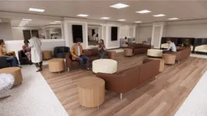 People sit and talk in the Surgical Family Waiting area with brown sofas, round tables, and wood-patterned flooring.