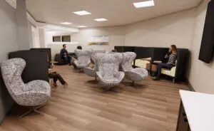 People relax and chat in stylish lounge chairs in a well-lit surgical family waiting area at Putney Memorial Hospital.