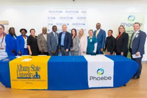 Twelve professionals stand behind a table with Albany State University and Phoebe Putney nursing program branding.