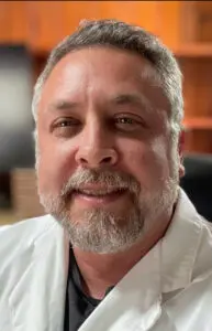 A middle-aged trauma surgeon with a graying beard, wearing a white lab coat.