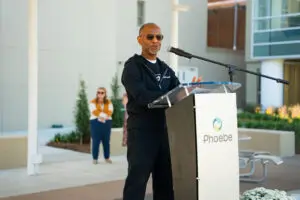 A man speaks into a microphone at an emergency podium branded with the Phoebe logo.