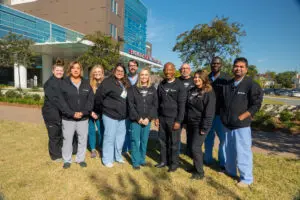 Ten medical professionals in black hoodies and scrubs standing in front of a Phoebe Level II Trauma Center.