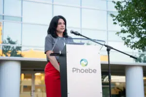 A woman speaks at a podium branded with the organization name Phoebe during a Wave of Light infant loss remembrance event.