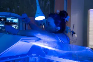 A healthcare worker at the hospital wears blue gloves while adjusting settings on an infant incubator screen.