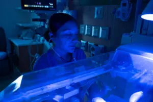 A healthcare worker in scrubs listens through a stethoscope while caring for an infant in a neonatal incubator at Phoebe.