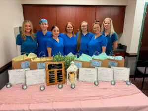 Seven nurse education staff from Phoebe stand behind a table displaying gift bags, certificates, and a commemorative plaque.