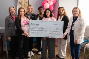 Six people stand together holding a large ceremonial donation check for the Carlton Breast Health Center.