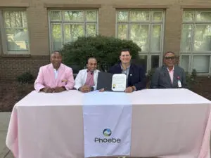 Four people sit at a table with a pink organization cloth during Breast Cancer Awareness month, one holding a signed document.