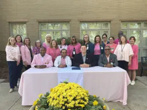A group in pink and professional attire poses behind a table during an Americus Breast Cancer Awareness Month proclamation.