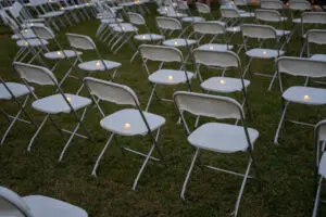 Rows of white folding chairs set up on grass, each with a lit candle for the Phoebe Wave of Light remembrance.