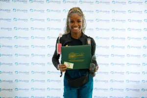 A nurse smiles while holding a DAISY Award folder and sculpture in front of a Sumter-branded step and repeat banner.