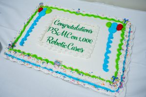 A rectangular cake with white icing, green and blue decorations, and a message celebrating Phoebe Sumter’s robotic procedures.